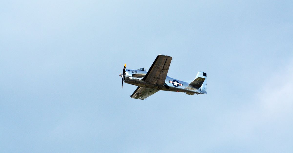 A vintage military aircraft flying solo against a clear blue sky, showcasing aviation history.